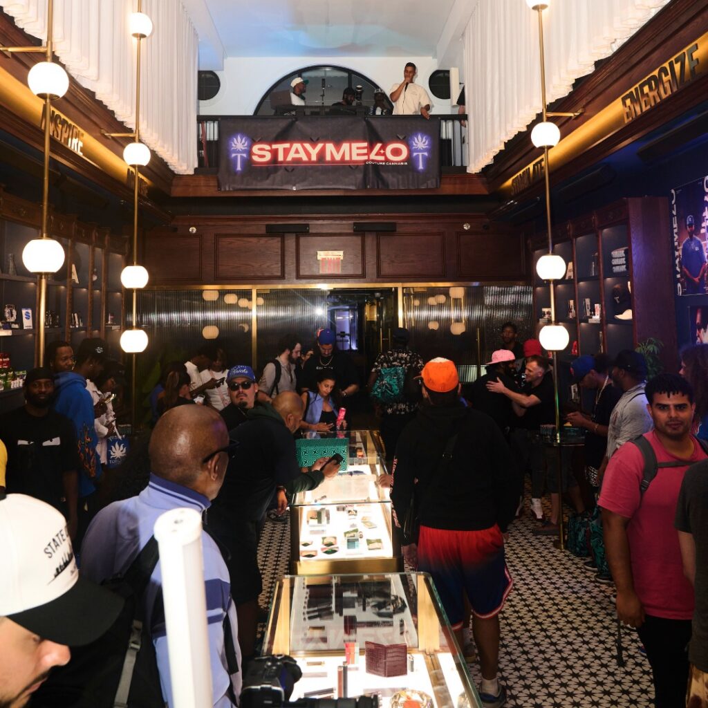 A bustling crowd inside a modern cannabis dispensary with a STAYME7O sign and products on display, evoking the sophisticated vibe of the Nat Sherman Townhouse.