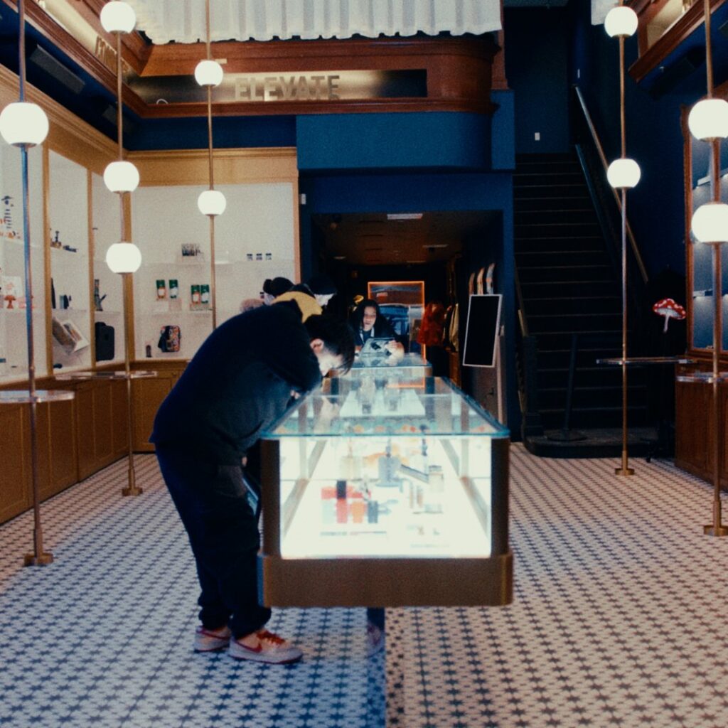 A person leans over a glass display case in the modern, well-lit Nat Sherman Townhouse, surrounded by tiled floors and hanging lights.