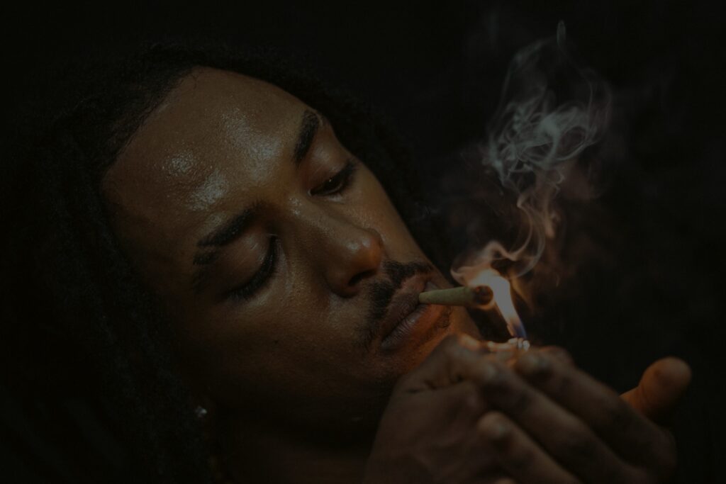 A person ignites a pre-roll with a lighter, exhaling fragrant smoke against a dark background.