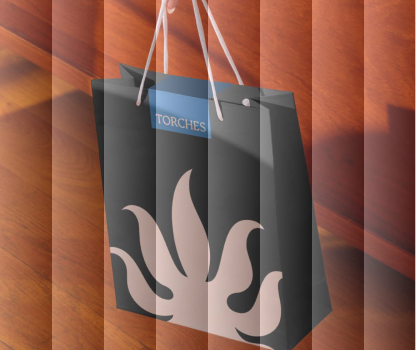 A black shopping bag with a flame design and TORCHES label, on a wooden floor.