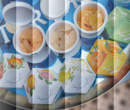 Colorful fruit-flavored gummies in open jars on a table with decorative boxes displaying fruit illustrations.