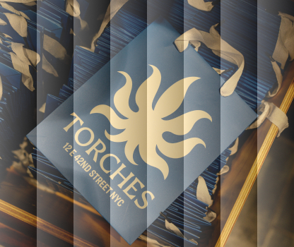 Blue brochure with a stylized torch logo and TORCHES 123 42nd Street NYC text, stacked with ribbon decorations.