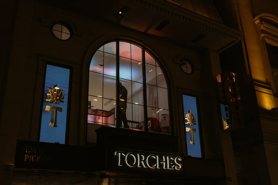 Exterior of a store named Torches with illuminated signs and a person visible through the upper window.