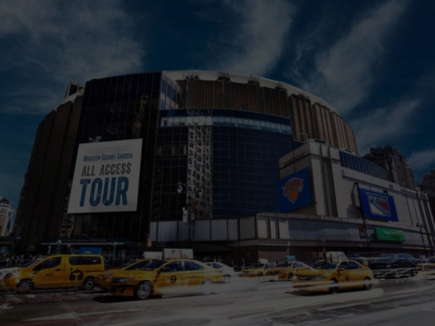 Exterior of Madison Square Garden with yellow taxis and a large banner promoting an all-access tour.