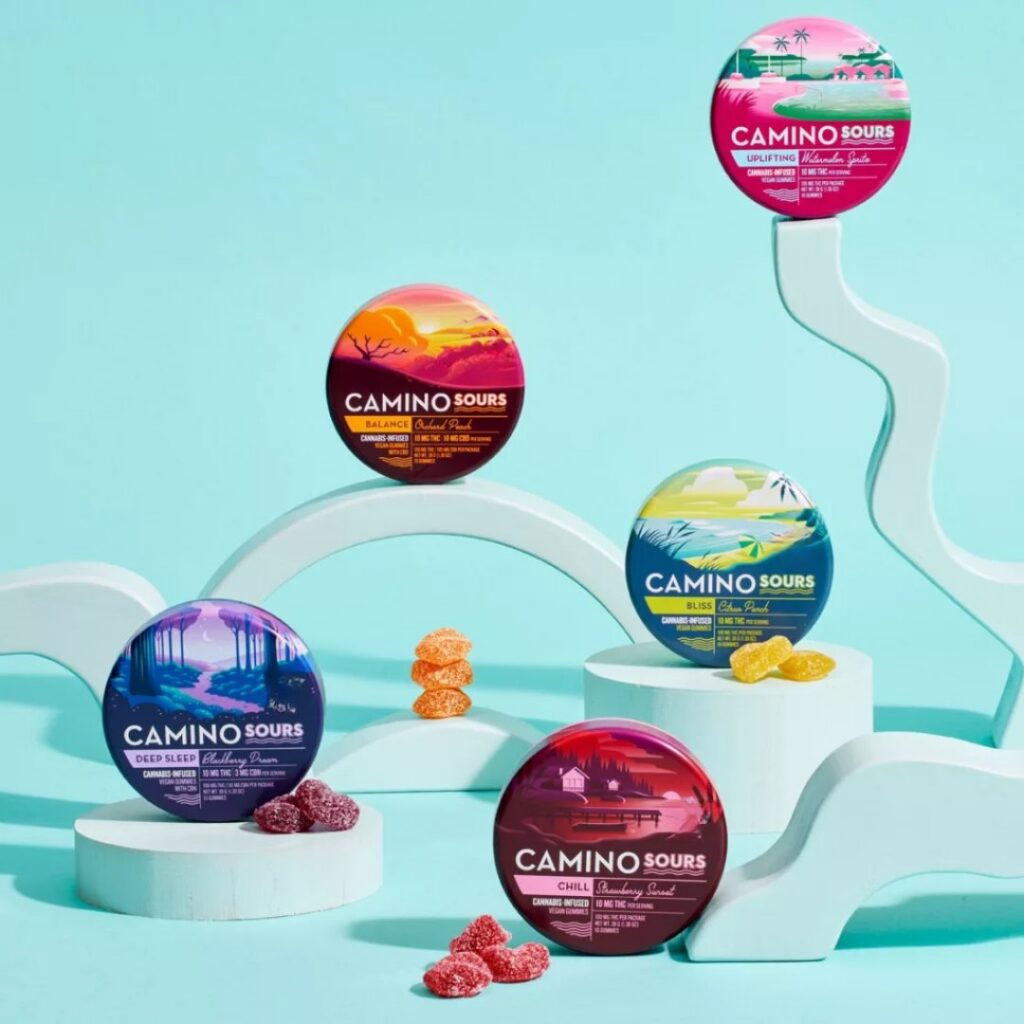 Five colorful Camino gummies tins, each filled with delicious sours, are artfully arranged on abstract pastel blue props.