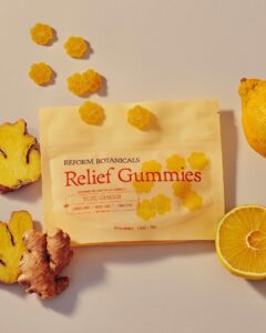 Yellow flower-shaped gummies, ginger root, yuzu fruit, and a yellow Relief Gummies package on a light surface.