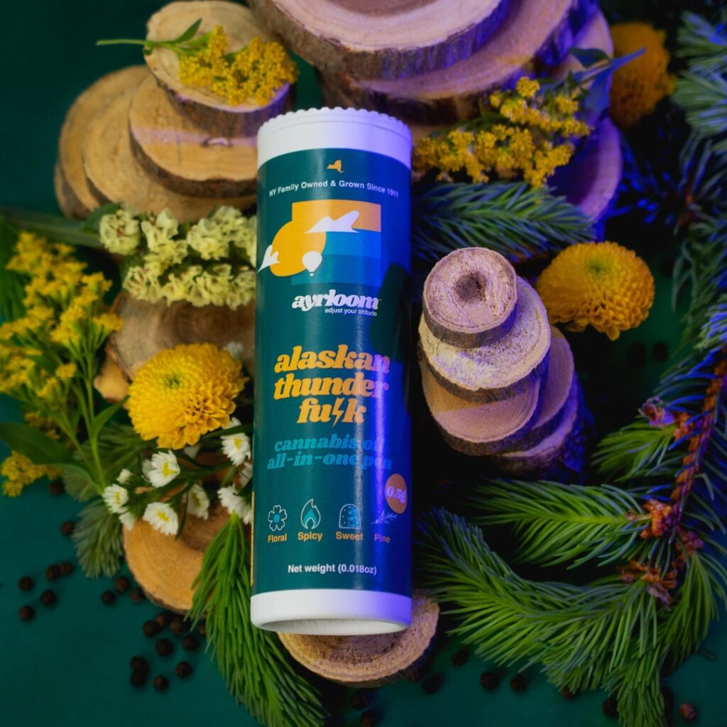 A cannabis product labeled alaskan thunder f**k on a green background with wood slices and greenery.