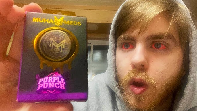 A surprised young man in a hoodie holds a Muha Meds Purple Punch vape cartridge box.