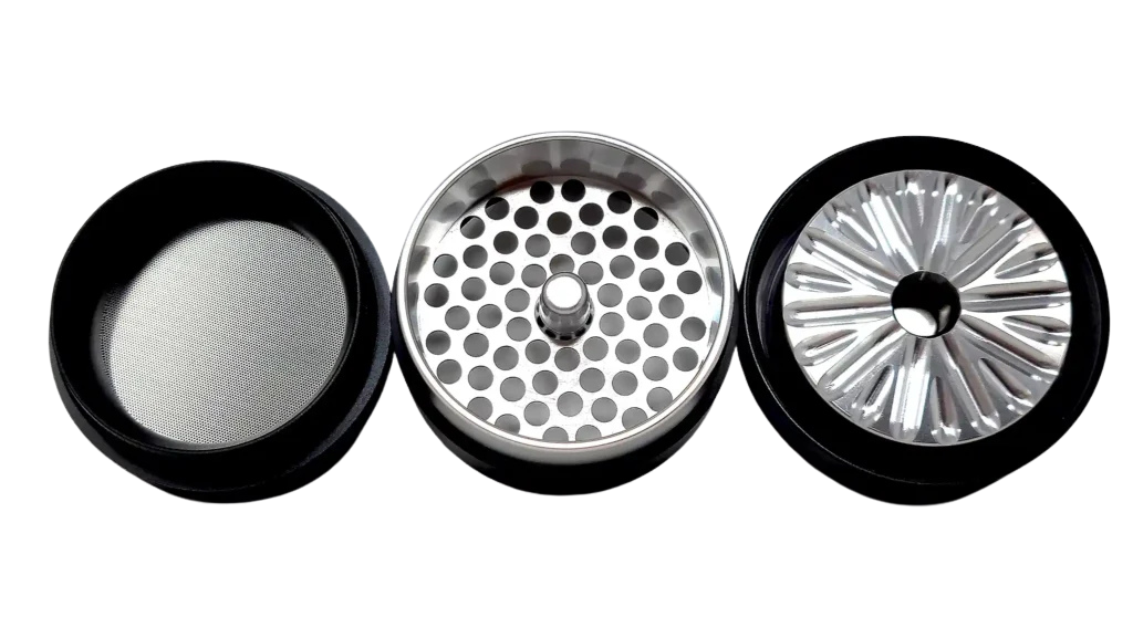 Three parts of a Flower Mill Grinder separated, showing mesh screen, grinding teeth, and holes for filtering.
