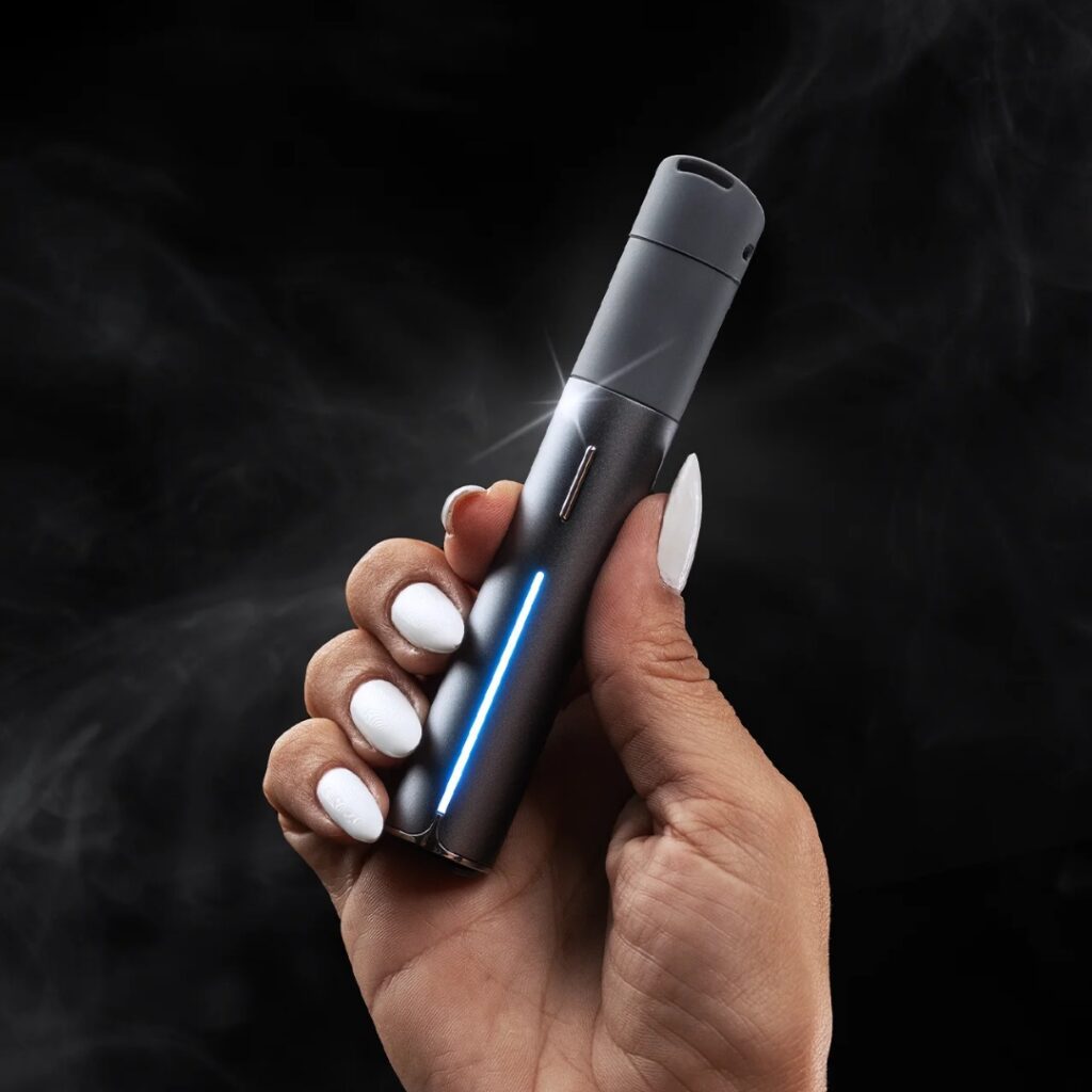 A hand with white nails holds a sleek, black vape pen with a blue LED light, surrounded by smoke.