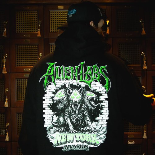 Person in a dark hoodie featuring the Alien Labs Brand and a green monster graphic on the back, standing by lockers.