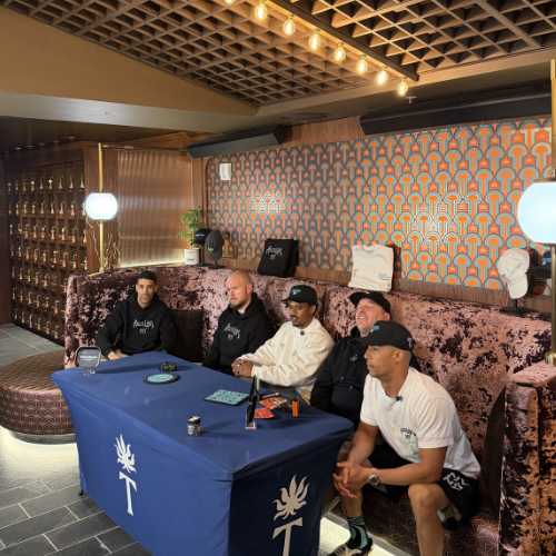 Five men sit at a blue table with Alien Labs Brand merchandise in a stylish, modern room with patterned walls and velvet seating.