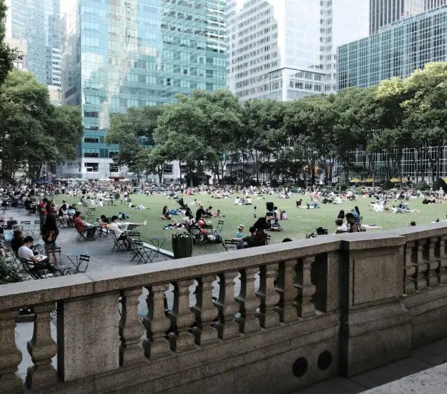 People relaxing on a grassy lawn surrounded by tall city buildings and trees on a sunny day.
