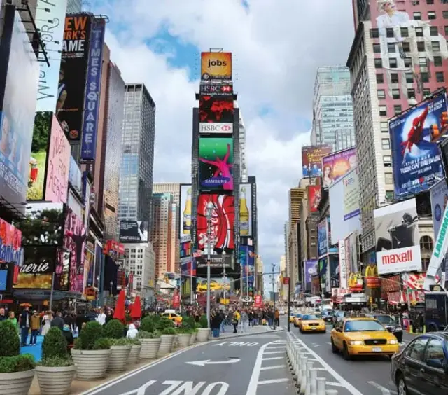 Busy Times Square in New York City with bright billboards, taxis, and crowds on a sunny day.