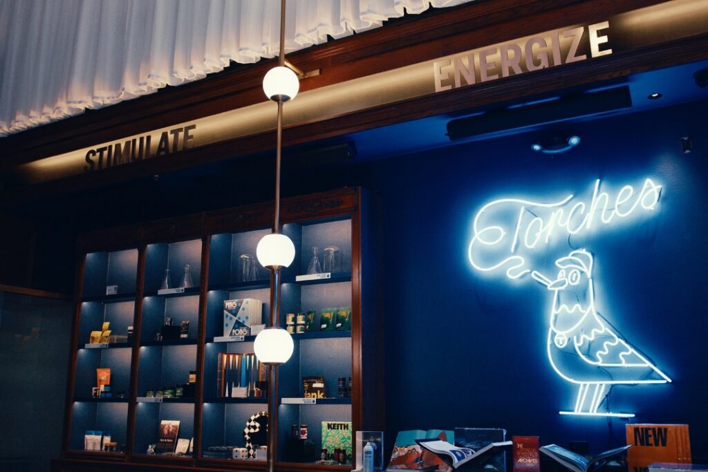 Neon bird sign reads Torches above a shelf of products, with STIMULATE and ENERGIZE signs above.