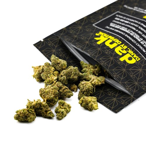 Small Grease Monkey Strain cannabis buds spilling out of a black and yellow branded packaging pouch onto a white surface.