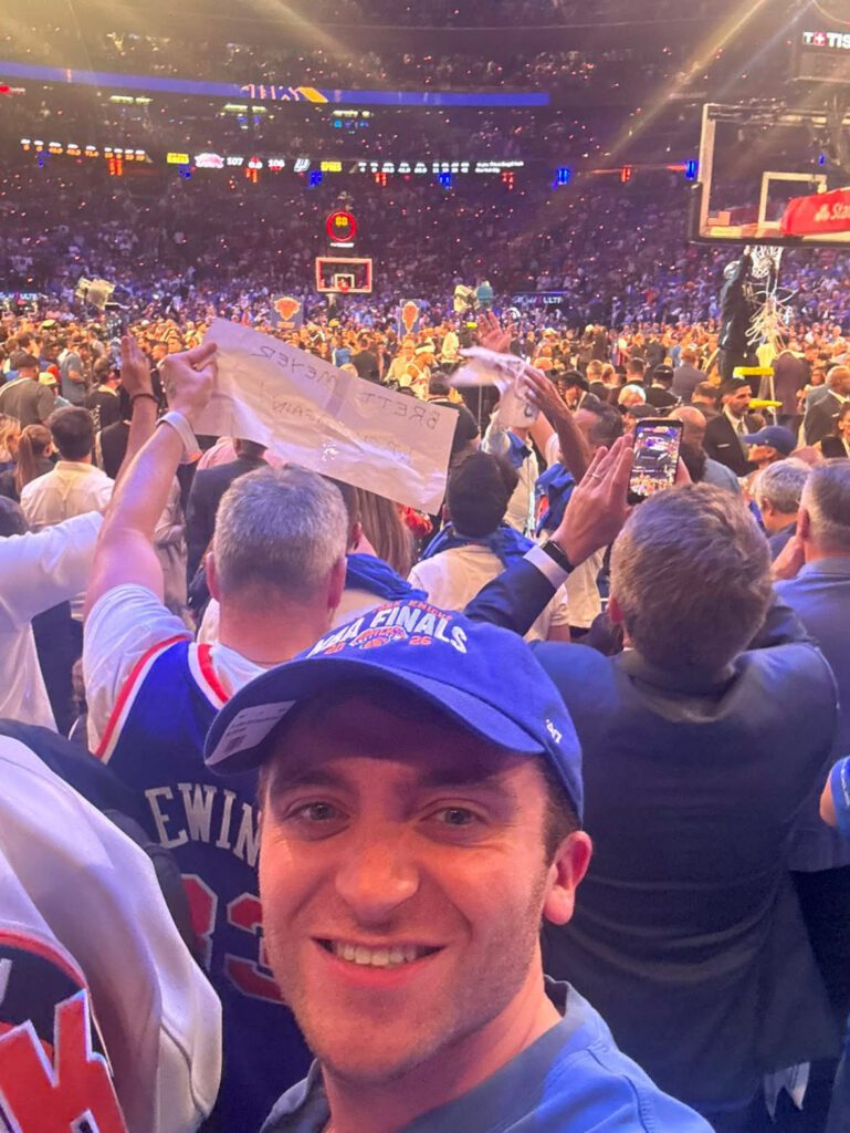 Man taking a selfie at a packed basketball arena during the Spurs vs Knicks game, with fans cheering in the background.