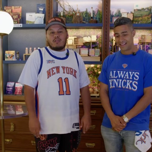 Two men in Knicks shirts stand indoors by shelves with various products and framed pictures, perhaps reminiscing about the latest Spurs vs Knicks showdown.