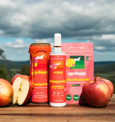 Red apples and apple products, including a jar, pouch, and spray bottle, are thoughtfully displayed on a wooden table outdoors—perfect for enjoying a crisp afternoon reminiscent of autumn gatherings at Torches NYC.