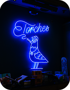 Blue neon sign of a bird smoking, with the word Torches above it, against a dark background.