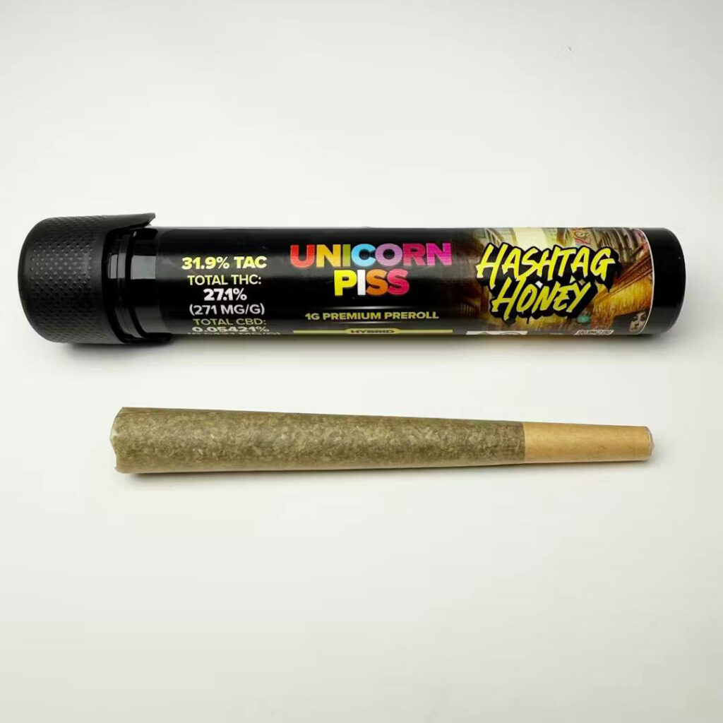 A pre-rolled joint and a labeled black tube reading Unicorn Piss Hashtag Honey on a white background.