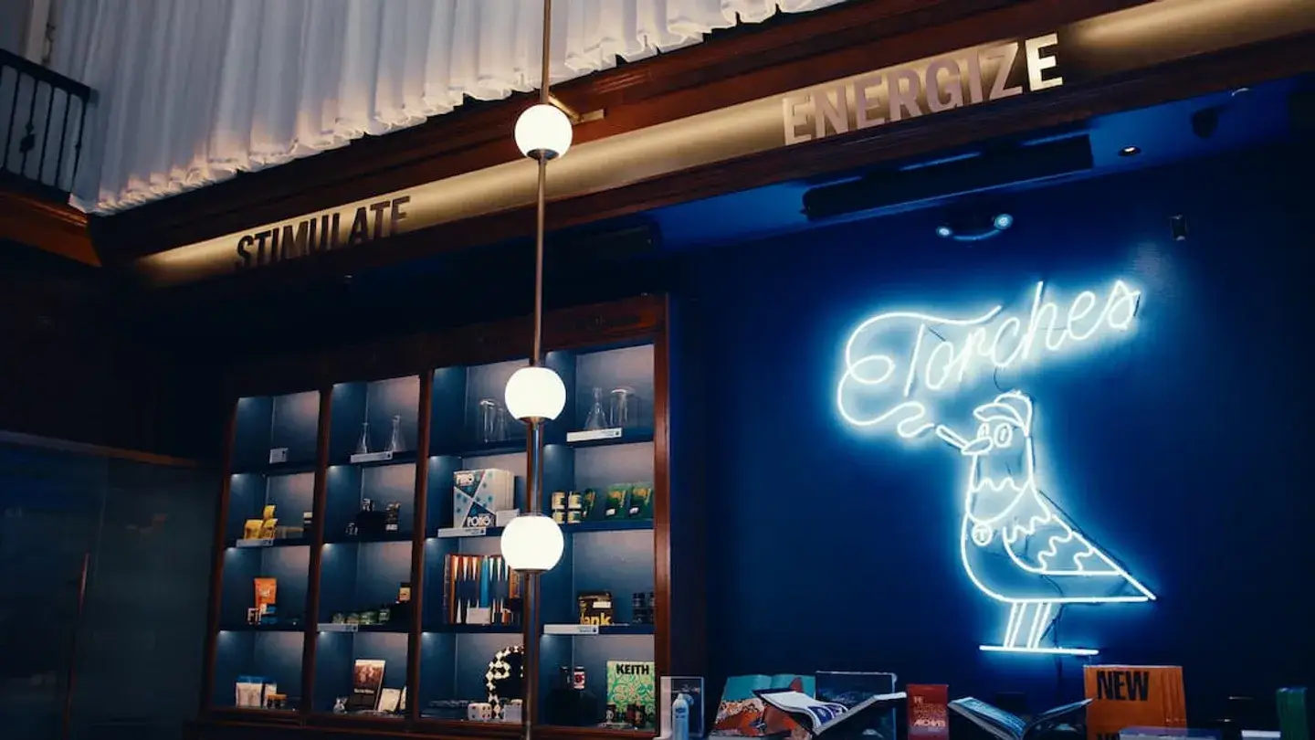 A neon bird sign reading Torches glows above products under ENERGIZE, STIMULATE, and hashtag honey signs.